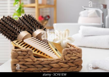 Hair styling. Different combs and brushes in wicker basket on white table in bathroom, closeup Stock Photo