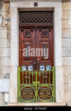 An ornate, dark wood double door with carved busts and a diamond-patterned transom is framed by stone and secured by a vibrant, weathered green wrough Stock Photo