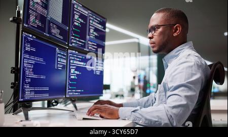 African American Man Coding On Multiple Computer Screens In Office. Stock Photo