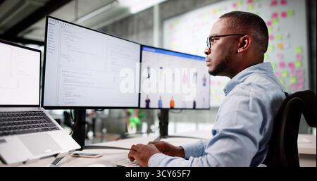 African American Man Coding Ecommerce Software On Multiple Office Monitors. Stock Photo