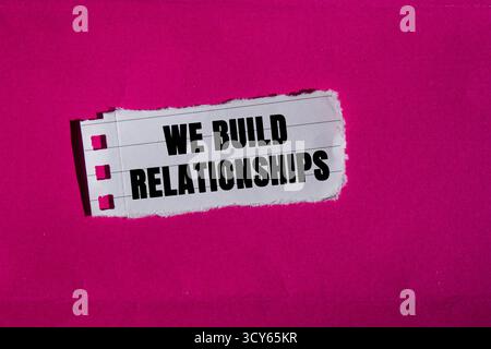 We Build Relationships message written on ripped torn lined paper piece on pink background. Conceptual We Build Relationships symbol. Copy space. Stock Photo