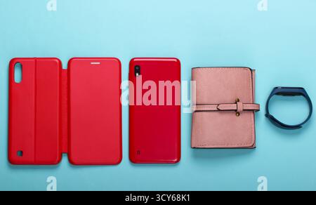 Smartphone with red leather protective case, wallet, smart bracelet on a blue background. Women's accessories. Top view Stock Photo