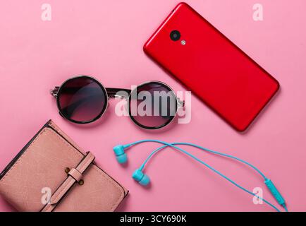 Women's accessories and gadgets on a yellow background. Earphones, stylish round sunglasses, smartphone, wallet on pink background Stock Photo