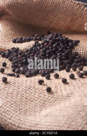 close-up of black peppercorns piled on burlap, dark spices on a rustic woven sack with warm lighting, natural ingredients and culinary spice concept Stock Photo