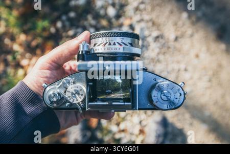 Top view of vintage 35mm film SLR camera with mine. male hands holding retro analog photo camera on forest background. Stock Photo