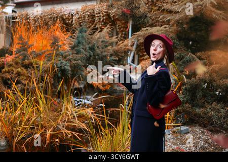 Surprised woman pointing at something in autumn garden, emotional travel moment outdoors Stock Photo