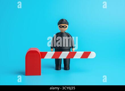 A masked thief behind a barrier gate. Stop crime. Cyber protection from hackers and industrial espionage. Security, data defense, and system integrity Stock Photo