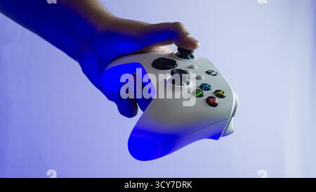 South Kalimantan, Indonesia - 07 14 2025 : White Xbox Series S|X controller held in one hand on white background under blue ambient light, showing min Stock Photo
