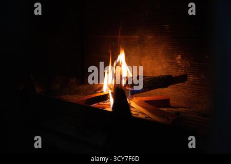 Close-up view of a flickering flame dancing above burning wood in a rustic fireplace. The flame displays intense shades of yellow, white with subtle b Stock Photo