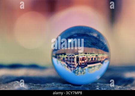 Glass sphere on a stone ledge showing an inverted view of buildings and trees, photographed with shallow depth of field using refraction in the ball. Stock Photo