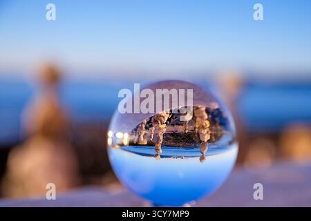 Crystal ball on a coastal ledge showing an inverted view of rock stacks and blue water in Lisbon, Portugal, captured at golden hour with shallow DOF. Stock Photo