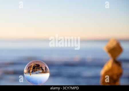 Lensball on a coastal wall showing an inverted view of a rocky shoreline and calm water in Lisbon, Portugal, captured near sunset with shallow DOF. Stock Photo