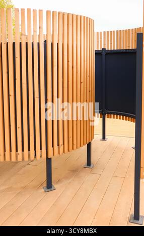 Outdoor beach changing cabin with curved wooden slats and dark panels modern public space architecture clean lines warm neutral tones vertical orienta Stock Photo