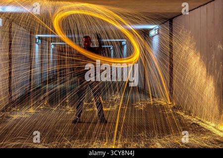 Steel wool spinning in tunnel creates vivid ring of sparks. Long exposure captures motion and contrast with blue lights. Stock Photo