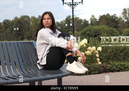 Young woman sitting alone on a park bench at dusk, looking distant and lost in thought, as if processing a recent breakup or emotional goodbye. Quiet Stock Photo