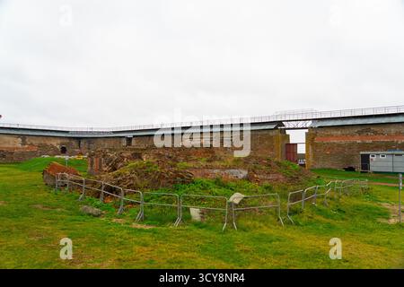Old stone and brick fortress walls, partially covered with grass, enclosing a central ruined area under a vast sky at Oreshek Fortress Stock Photo