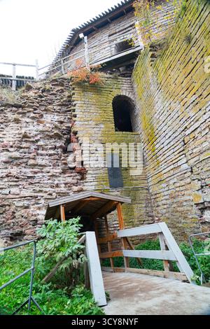 A massive, angled stone fortress wall with a memorial plaque, an archway, and a wooden shelter and ramp leading up the slope at Oreshek Fortress Stock Photo