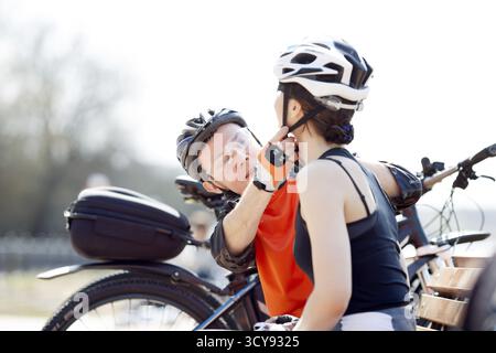 Woman, man sitting on bench putting on helmet in park Stock Photo