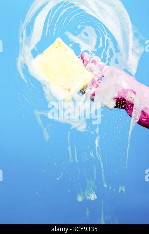 Person with foam sponge washes window on blue background Stock Photo