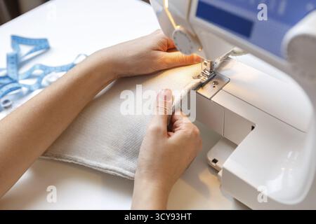 Woman sews fabric on machine sitting indoors Stock Photo