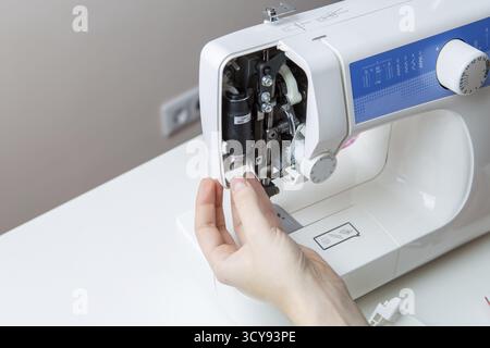 Young man repairing sewing machine standing on blank gray background Stock Photo