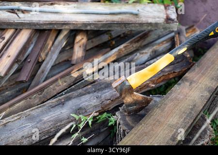 Axe with yellow handle embedded in wooden boards outdoors. Concept of manual labor and woodworking tools. Stock Photo