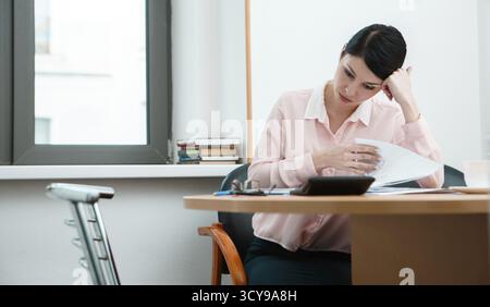 Young businesswoman sitting at workplace and reading paper in office Stock Photo