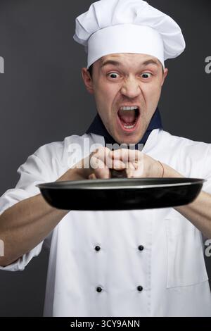 Angry chief in uniform holding pan isolated on grey Stock Photo