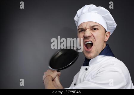 Angry chief in uniform threaten by pan isolated on grey Stock Photo