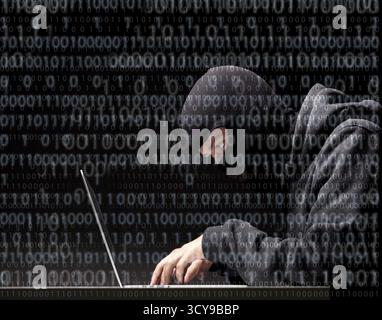 Computer hacker in a balaclava working in the darkness stealing data and personal identity information off a laptop computer Stock Photo