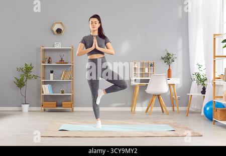 Young yogi sporty attractive woman practicing yoga at home, doing Vrksasana exercise, Tree pose Stock Photo