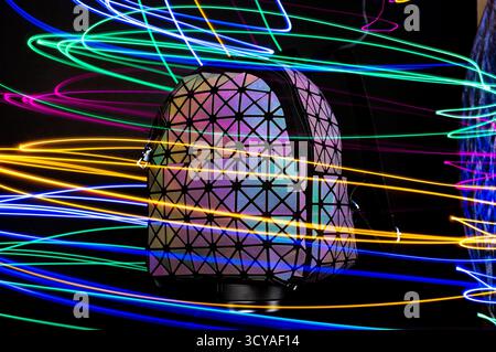 A bright multicolored backpack on a black background. Multicolored, bright, glowing lines. Bag and illumination. Front view. Stock Photo