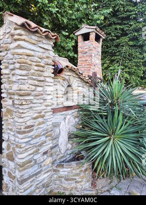a stone outdoor stove next to a sprawling yucca bush in the shade of garden trees. Mediterranean comfort Stock Photo