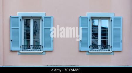 Pastel Pink Building Facade with Blue Shuttered Windows and Iron Railings Stock Photo