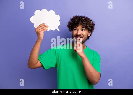 Positive man in green t-shirt holding paper speech bubble on violet background, expressing thoughts and optimism Stock Photo