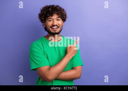 Positive man in green shirt pointing and smiling against purple background, illustrating friendly and confident lifestyle Stock Photo