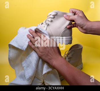 beige canvas boot being cleaned by hands against bright yellow background in studio Stock Photo