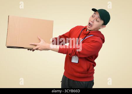 delivery courier in red hoodie lifts cardboard box with surprised expression Stock Photo