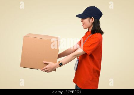 delivery worker lifting package cardboard box in red uniform and cap for parcel delivering to you Stock Photo