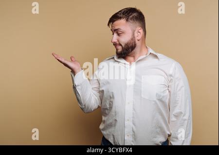 A man stands confidently against a plain light background. He wears a white shirt and looks to his left while gesturing with his hand to express a poi Stock Photo