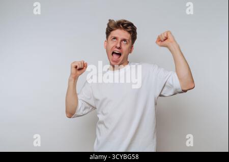 A young man with short curly hair is joyfully celebrating with raised fists. He has a big smile on his face, expressing excitement and enthusiasm in a Stock Photo