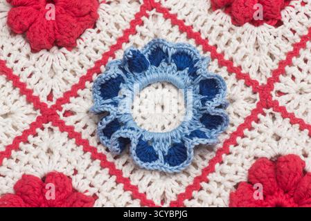 Vibrant crochet pattern with red and central blue flower on white Stock Photo