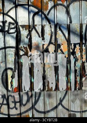 Close-up of a metal wall with layers of peeling graffiti showing various colors and textures in an urban setting Stock Photo