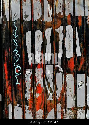 Close-up of grungy urban wall with peeling paint and graffiti in white, red, and black colors giving a distressed look Stock Photo