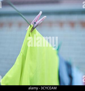 Bright green shirt hanging on clothesline with pink clothespin in outdoor setting. Stock Photo