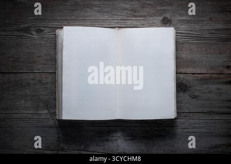 An old open book with blank white pages lies flat on a dark, rustic wooden table. Stock Photo