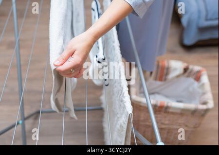 Close-up of female hands hanging clean laundry on drying rack, concept of home chores and domestic routine Stock Photo