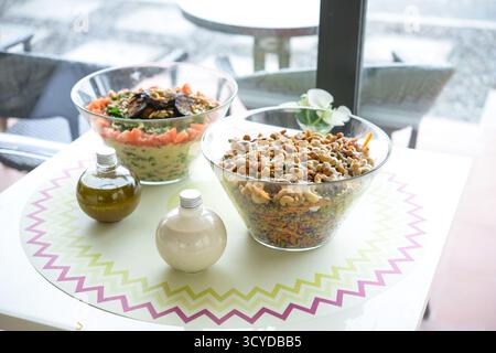 Assorted Salads in Glass Bowls include grains, vegetables, and nuts served on a table with dressing bottles side view Stock Photo