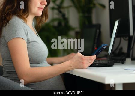 Pregnant woman working diligently on laptop, capturing the challenge of maintaining career while expecting. Natural facial expression shows mild exhaustion and focus. Stock Photo