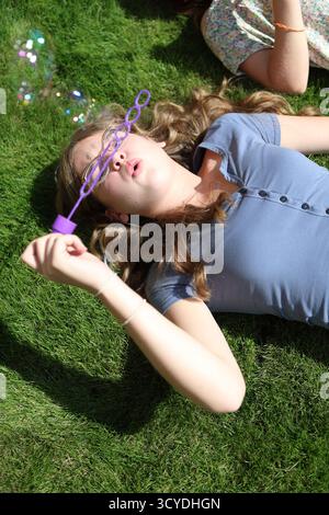 Girls blowing bubbles with liquid soap lying on grass lawn Stock Photo